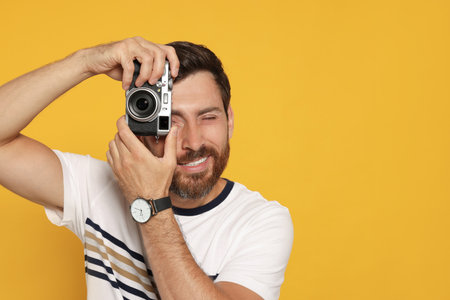 Man with camera taking photo on yellow background, space for text. interesting hobbyの写真素材