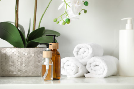 Bottles with dispenser caps, houseplant and towels on white table in bathroomの写真素材