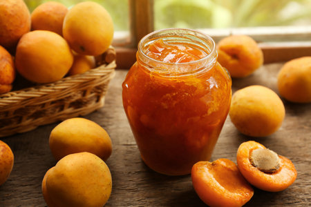 Jar of delicious jam and fresh ripe apricots on wooden table indoors. fruit preserveの写真素材