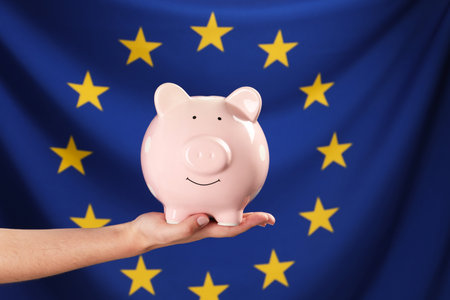 Woman holding pink piggy bank against flag of European Union, closeupの写真素材