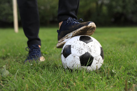 Man with dirty soccer ball on green grass outdoors, closeup
