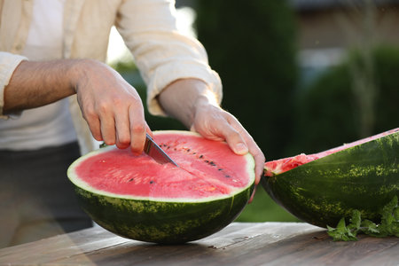 Man cutting tasty ripe watermelon at wooden table outdoors, closeupの写真素材