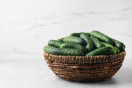 Fresh ripe cucumbers in wicker basket on marble table, space for textの写真素材