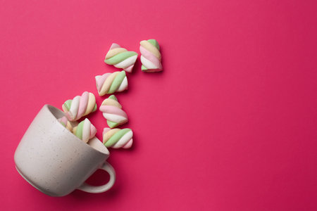 Overturned cup with delicious colorful marshmallows on crimson background, flat lay. Space for textの写真素材