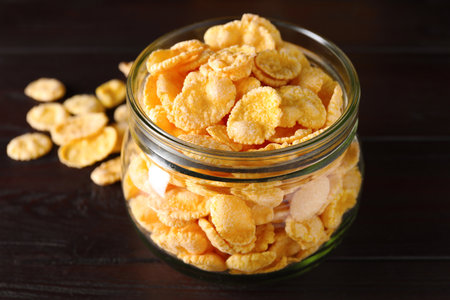 Jar of tasty crispy corn flakes on wooden table, closeup