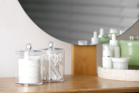 Containers with cotton swabs and pads near cosmetic products on dressing tableの写真素材