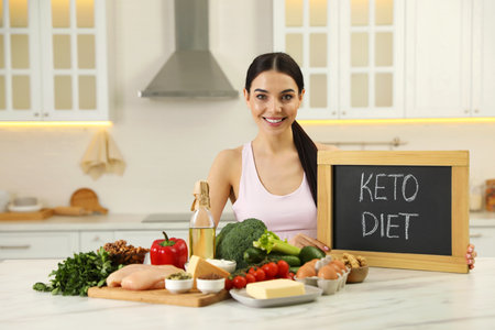 Happy woman holding chalkboard with words Keto Diet near different products in kitchenの写真素材