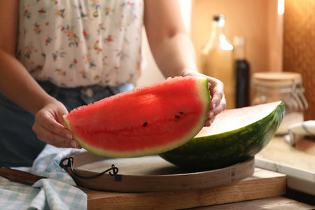 Woman holding slice of fresh juicy watermelon on wooden table, closeupの写真素材