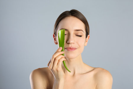 Young woman with aloe leaf on light gray backgroundの写真素材