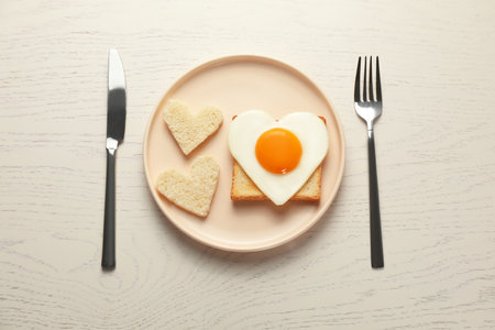 Heart shaped fried egg served on white wooden table, flat layの写真素材