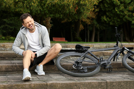 Man with injured knee on steps near bicycle outdoorsの写真素材