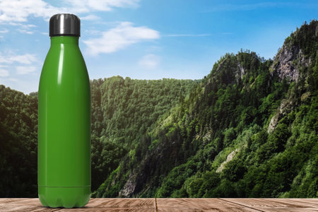 Green bottle thermo on wooden table and beautiful view of mountains, space for textの写真素材