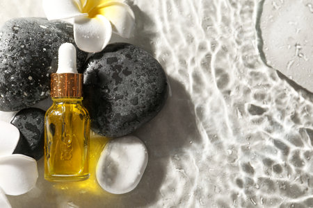Bottle of face serum and spa stones in water on light background, flat lay. Space for textの写真素材
