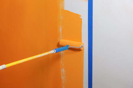 Person painting wall with roller and orange dyeの写真素材