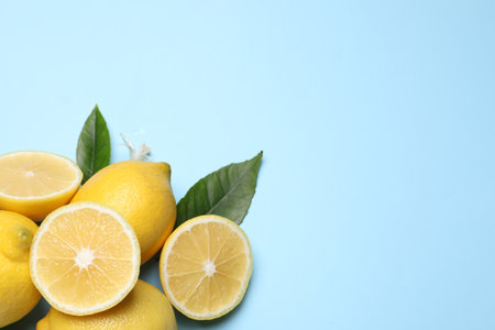 Many fresh ripe lemons with green leaves and flower on light blue background, flat lay. Space for textの写真素材