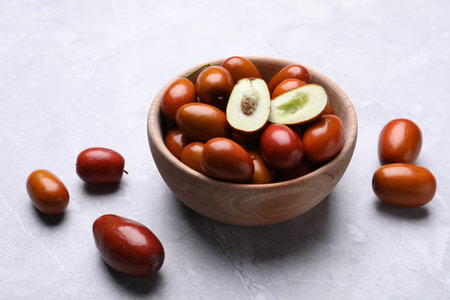 Fresh Ziziphus jujuba fruits with wooden bowl on light tableの写真素材