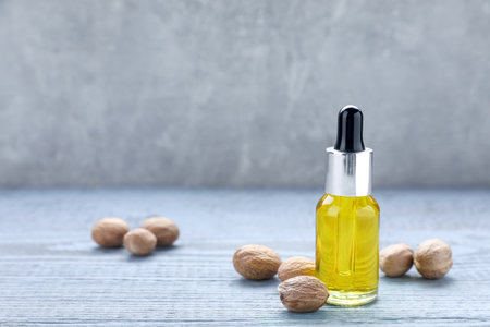 Bottle of nutmeg oil and nuts on gray wooden table. Space for textの写真素材