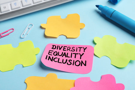 Sticky note with words Diversity, Equality, Inclusion and paper puzzle pieces on light blue...