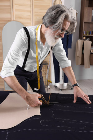 Professional tailor cutting fabric by following chalked sewing pattern at table in workshopの写真素材