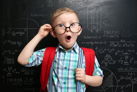 Funny little child wearing glasses near chalkboard with different formulasの写真素材
