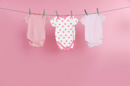 Baby clothes drying on laundry line against pink backgroundの写真素材