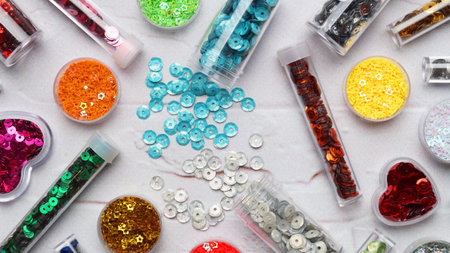 Many different colorful sequins in containers and tubes on marble e background, flat lay