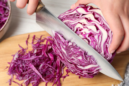 Woman cutting fresh red cabbage on white wooden table, closeup