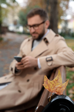 Handsome man wearing stylish clothes in autumn park, focus on yellow leafの写真素材
