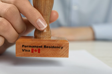 Woman stamping document on white wooden table, closeup. Permanent residency visa in Canada