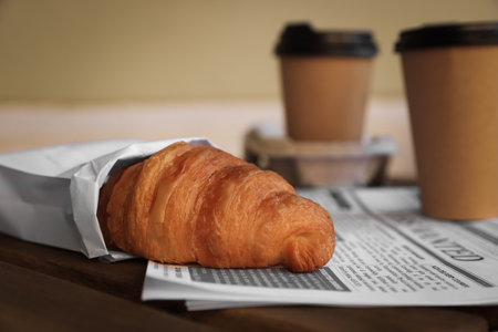 Tasty croissant, newspaper and paper cups of coffee on wooden table, closeupの写真素材