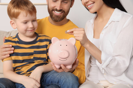 Happy family putting coin into piggy bank indoors, closeupの写真素材