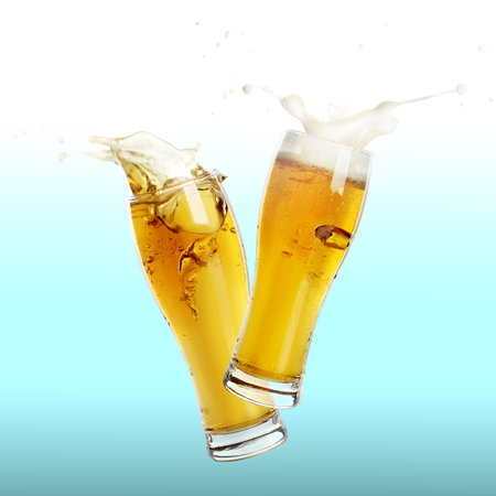 Two glasses of beer toasting with splash on color backgroundの写真素材