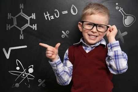 Cute little child wearing glasses near chalkboard with chemical formulasの写真素材