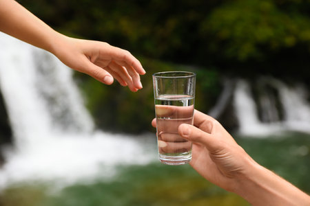 Man giving woman glass of fresh water near waterfall, closeupの写真素材