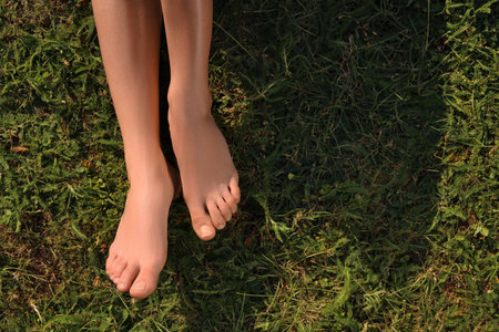 Woman sitting barefoot on green grass outdoors, top view. Space for text