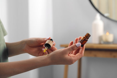 Young woman applying essential oil on wrist indoors, closeupの写真素材