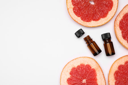 Bottles of citrus essential oil and fresh grapefruit slices on white background, flat lay. Space for textの写真素材