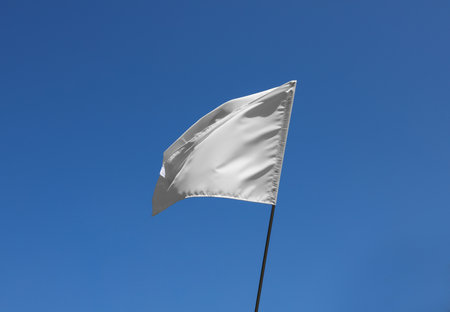White flag fluttering against blue sky on sunny dayの写真素材