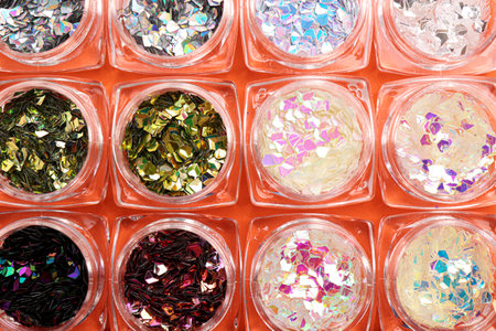Jars with colorful shiny glitter on orange background, flat lay