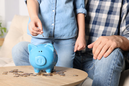 Little girl with her father putting coin into piggy bank at home, closeupの写真素材