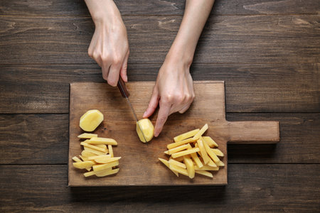 Woman cut potatoes on wooden table, top viewの写真素材