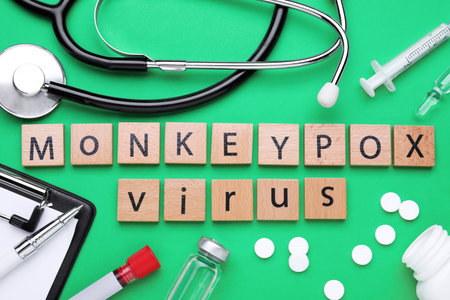 Flat lay composition with words Monkeypox Virus made of wooden squares and medical supplies on green...
