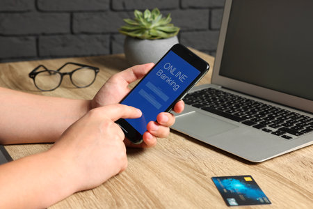 Man using online banking app on smartphone at wooden office table, closeup