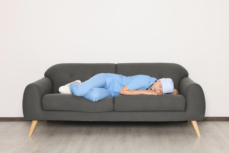 Tired young doctor sleeping on sofa indoorsの写真素材