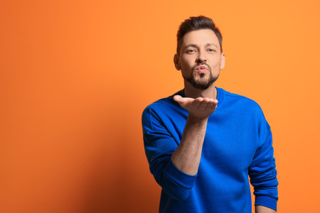 Handsome man blowing kiss on orange background. Space for textの写真素材