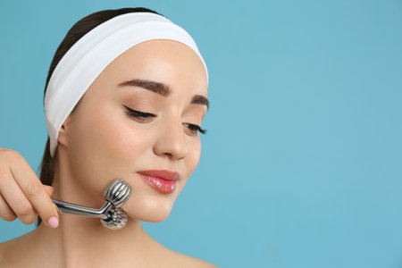 Woman using metal face roller on light gray background, space for text