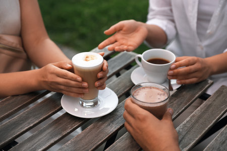 Friends drinking coffee and cocoa at wooden table in outdoor cafe, closeupの写真素材