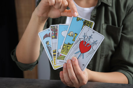 Fortune teller with tarot cards at gray table indoors, closeup