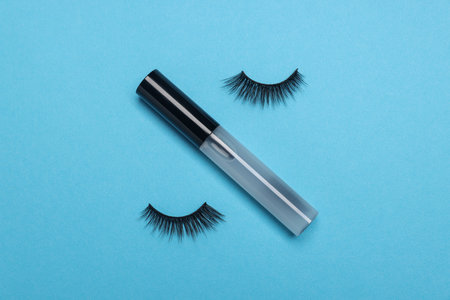 False eyelashes and tube of oil on light blue background, flat layの写真素材