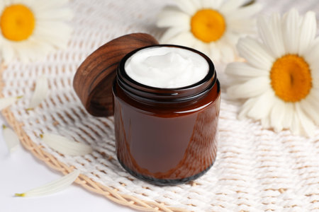 Glass jar of face cream and beautiful flowers on white tableの写真素材